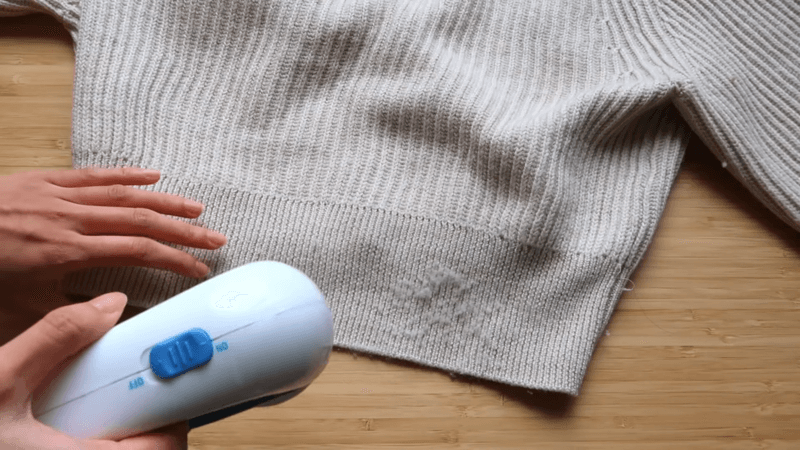 a woman's hand holding hairdryer cleaning an embroidered sweatshirt