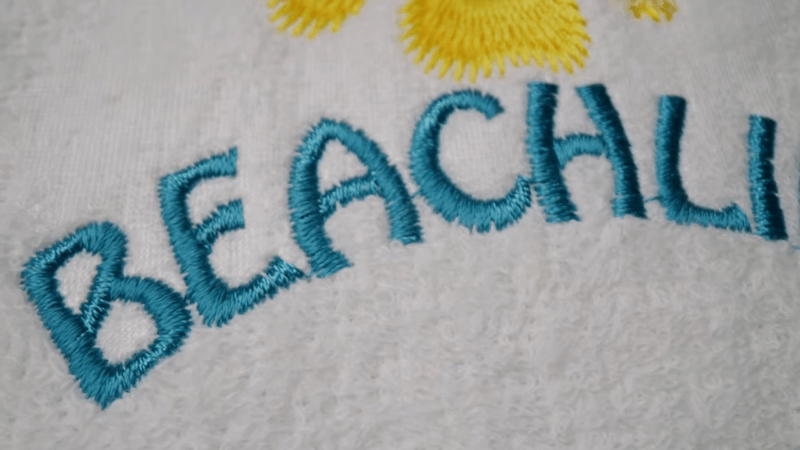 white fabric with yellow pattern and blue embroidered text beachlif