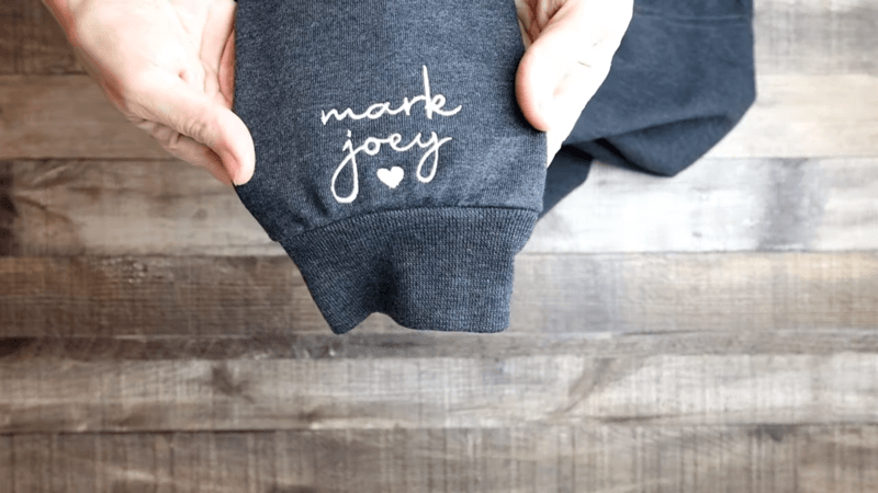 hands holding a black embroidered sweatshirt sleeve with text marle joey